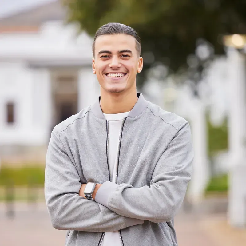Smiling young man with arms crossed standing outdoors near a white building.