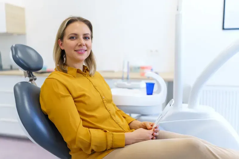 Woman in mustard shirt smiling while seated in a dental chair.